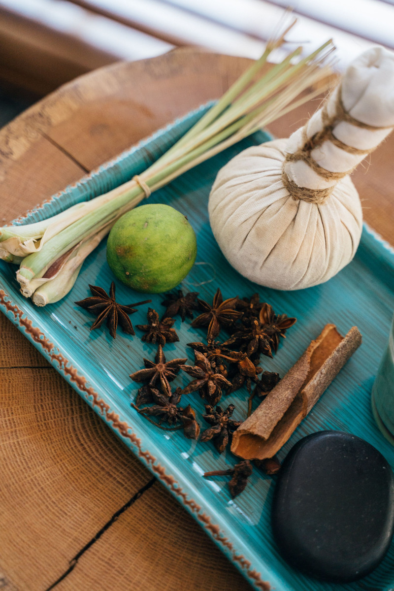 A tray with a herbal potli, lemongrass, lime, star anise, cinnamon and a dark soap.