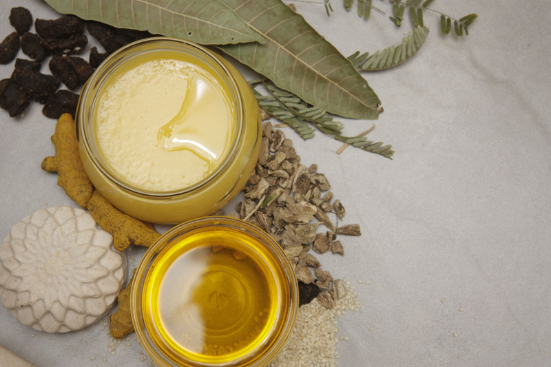 Ghee and warm oils in glass jars with turmeric and dried herbs.